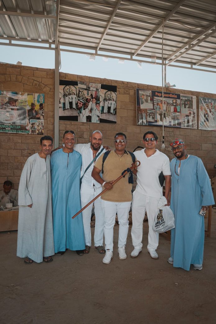 Grupo de seis personas posando juntas bajo una techumbre metálica, algunas con túnicas locales.