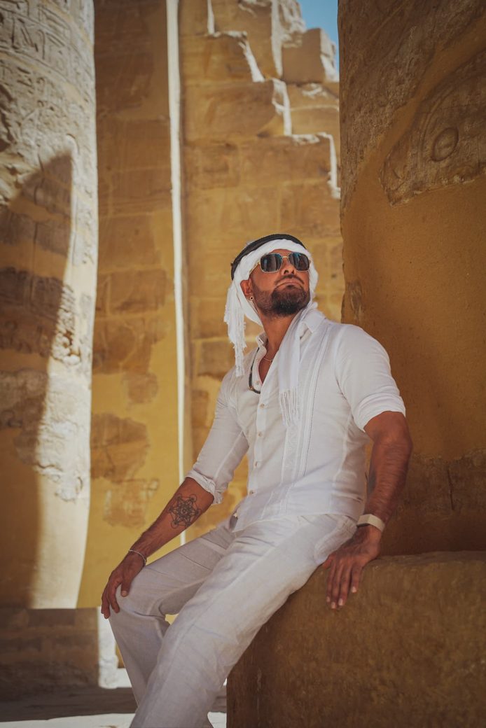 Ricardo Ponce vestido de blanco, sentado entre columnas de piedra iluminadas por el sol.