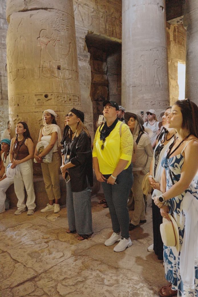 Grupo de participantes de pie entre columnas grabadas, mirando hacia el techo del templo.