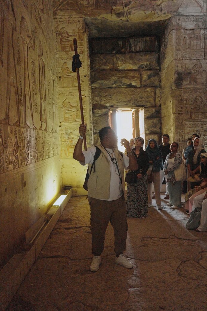 Guía señalando relieves de un muro interior del templo mientras el grupo escucha en el pasillo.